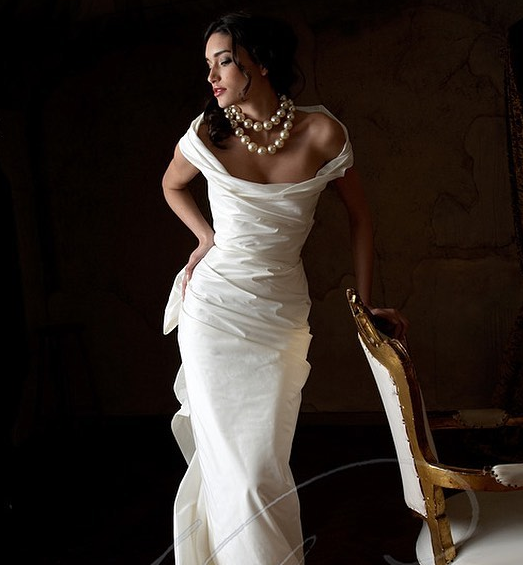The Bride in fitting wedding dress from plain white fabric, huge pearl necklace, classic updo