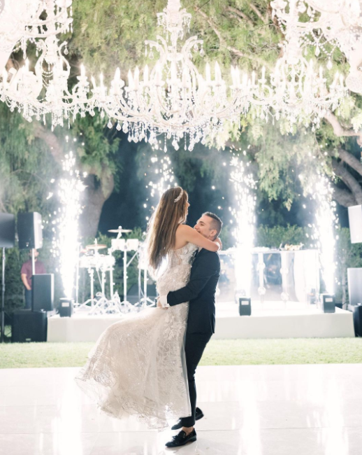 Crystal chandeliers on the trees, white fireworks, wedding couple in glamour wedding outfits, scene in the back