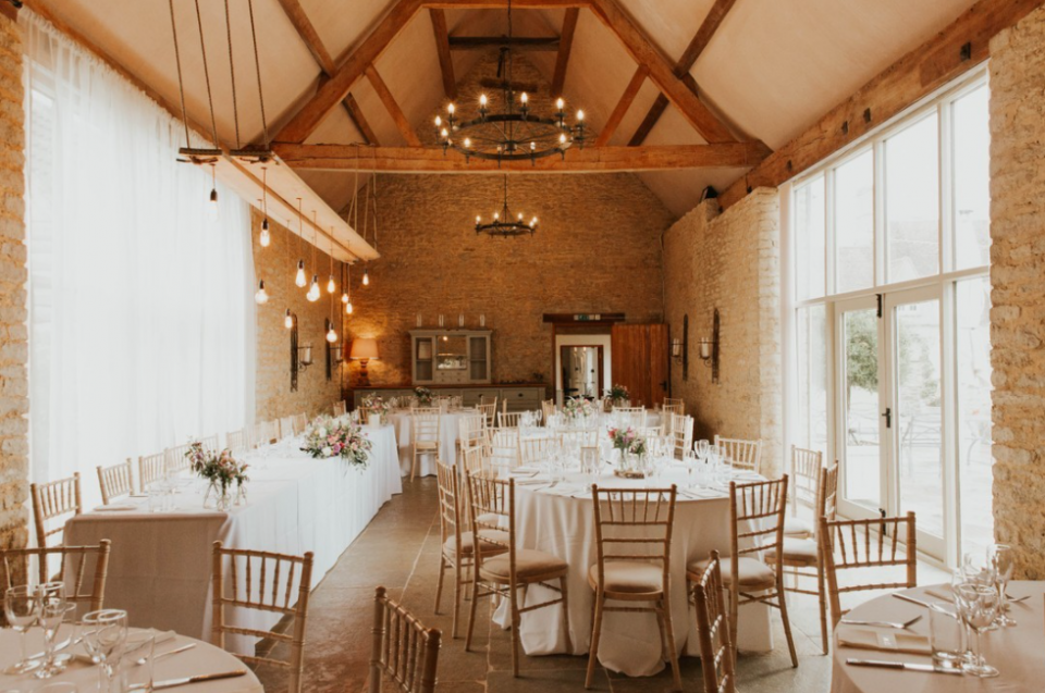 Red brick barn with wooden construction roof, metal round chandeliers, Edison bulbs, round reception tables with pastel flower arrangements