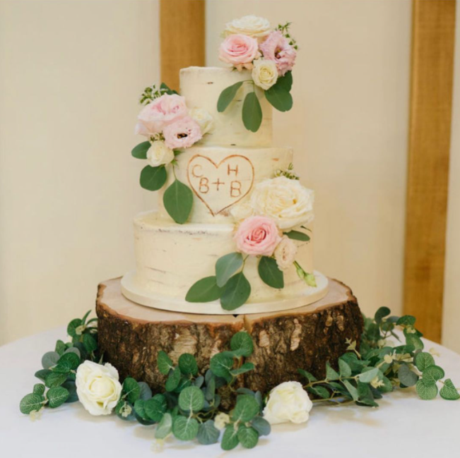 Wedding cake three level resembling birch tree stump decorated with white and pink roses and engraved newly-weds initials looking like carvings in the wood