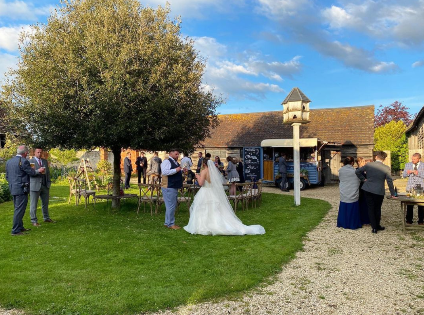 Countryside farm, barn wedding party outdoors, pigeon feeding station, olive tree, snack van in the background, guests chatting