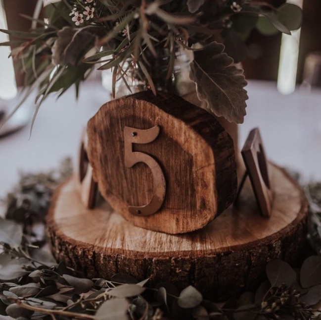 Wooden sign with table number 5 made out of tree ring and metal number placed on bigger tree ring