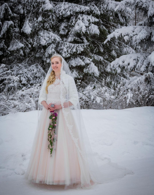 Blonde Bride on the snow, pine trees behind covered in snow