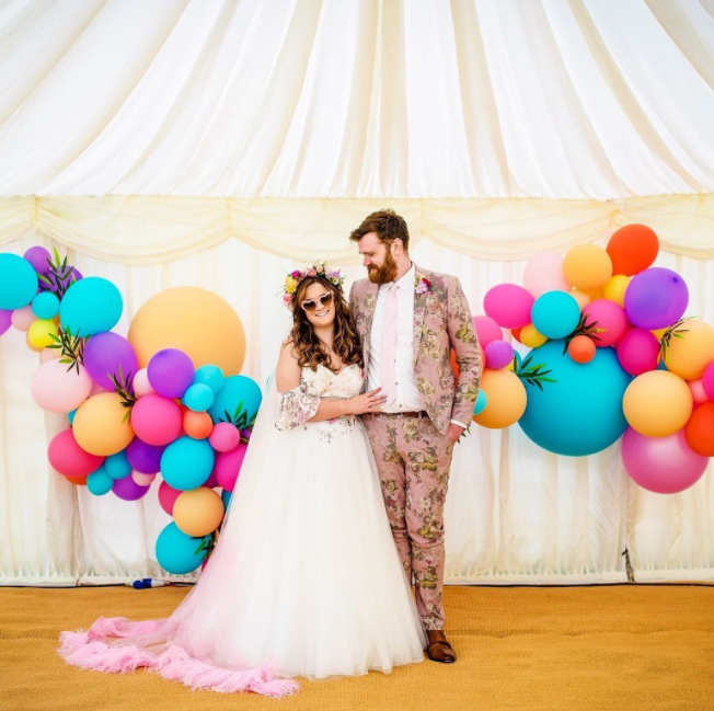 Smiling wedding couple, pink suit, colorful baloons, carnival tent