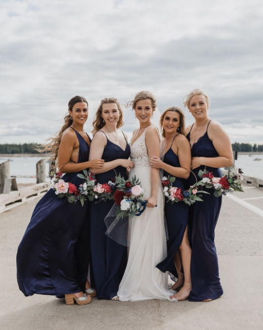 The Bride with bridesmaids in dark blue dresses on the bridge by the sea