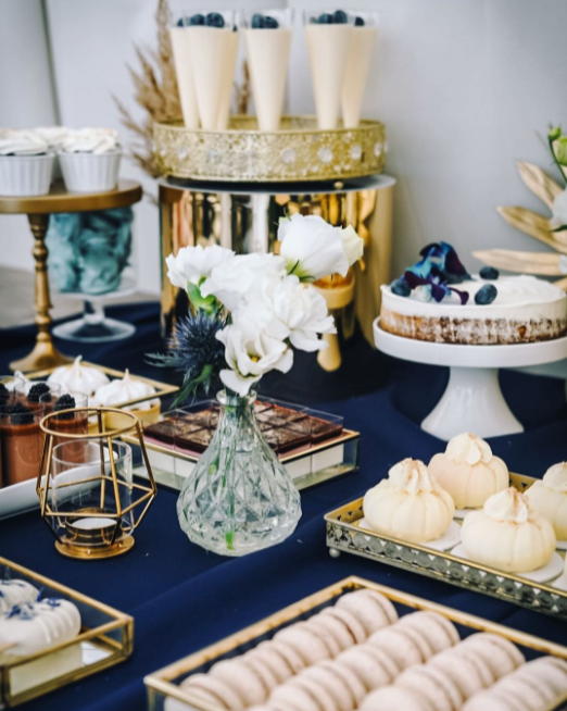 Wedding snack table decoration with geometrical shapes, golden and dark blue color, macaroons, blueberry cake, crystal vase