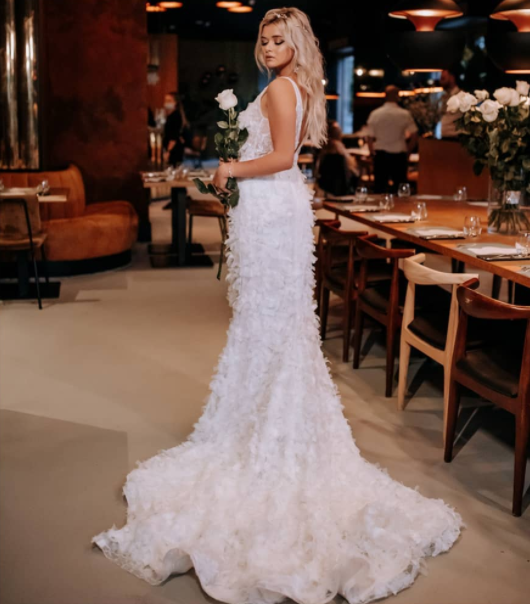 Blonde bride in long feather white dress with white rose in hand