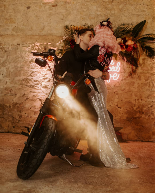 Couple on motorcycle, silver dress, pink hair in pin up hairstyle, neon lights and flowers on the wall