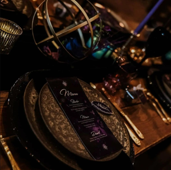Old wood table, black ornamented plates, deep purple and dark blue decor with sphere with dried flowers inside