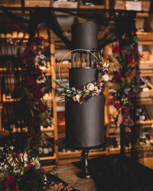 3 levels black wedding cake decorated with golden circle and pastel colored flowers