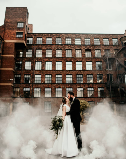 Wedding couple kissing in the smoke, red brick factory with huge windows in the background