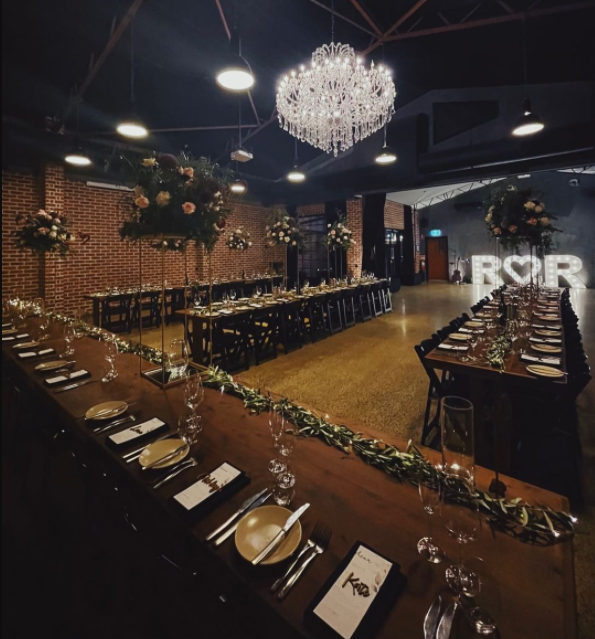 Dark industrial wedding venue with long wooden tables, crystal chandelier on the high ceiling