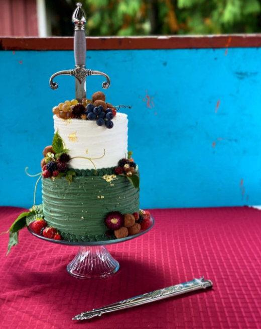 Two levels white and green wedding cake decorated with fruits with a sword put inside the cake