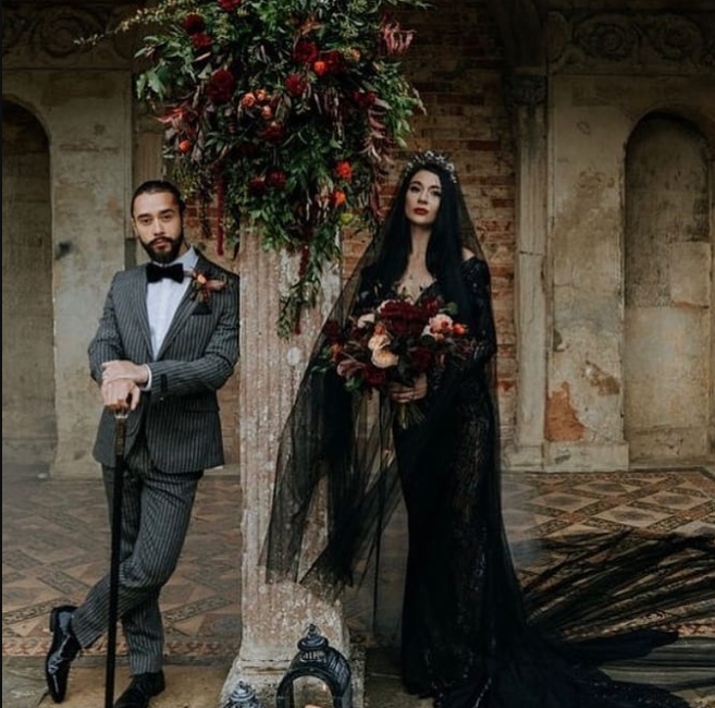 Wedding couple under the castle pillar, the bride in black wedding dress and long black veil, the Groom in striped suit with cane in his hands