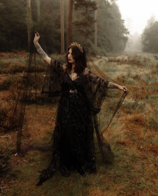 Laced, airy black wedding dress on the tattooed girl on the meadow