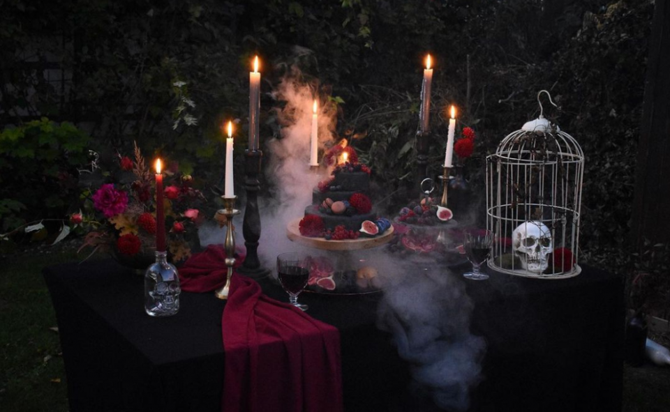 Black table cloth with red table runner, black wedding cake, birdcage with a skull inside, long white candles, red flowers