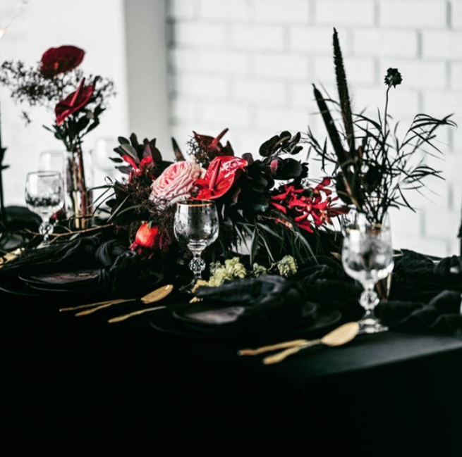 Dark greenery with red flowers, glasses and black table cloths