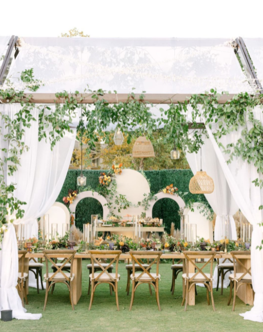 Wedding venue made out of wood and fabric, wedding wooden table and chair in the garden, leaves decoration and wicker lamps