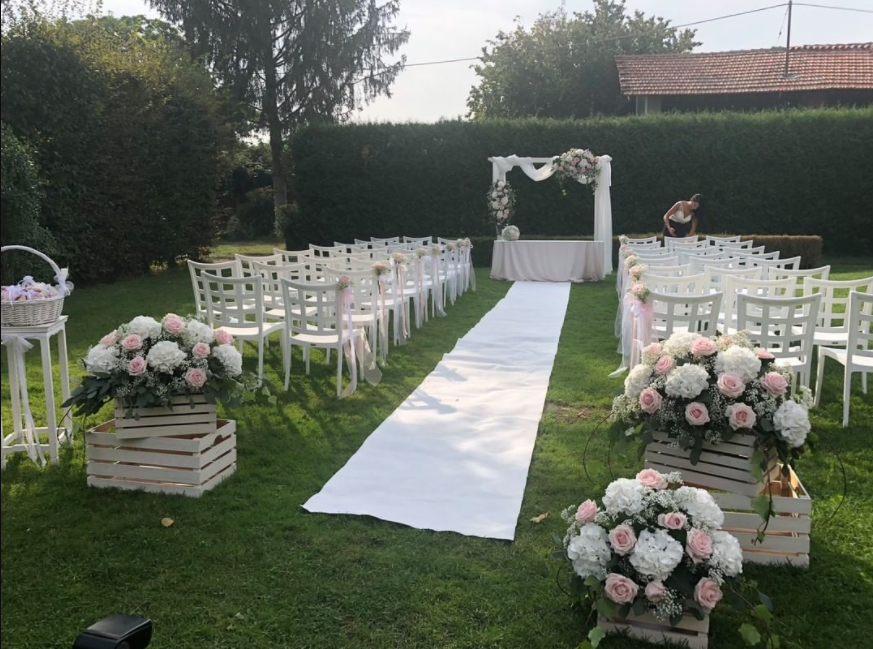 Wedding reception venue with white chairs, pastel bouquets in white crates and white carpet on the green grass