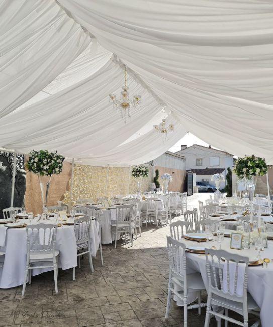 White fabric roof with crystal chandeliers, round tables with plain white table cloths, white wooden chairs and bouquets in high glass vases