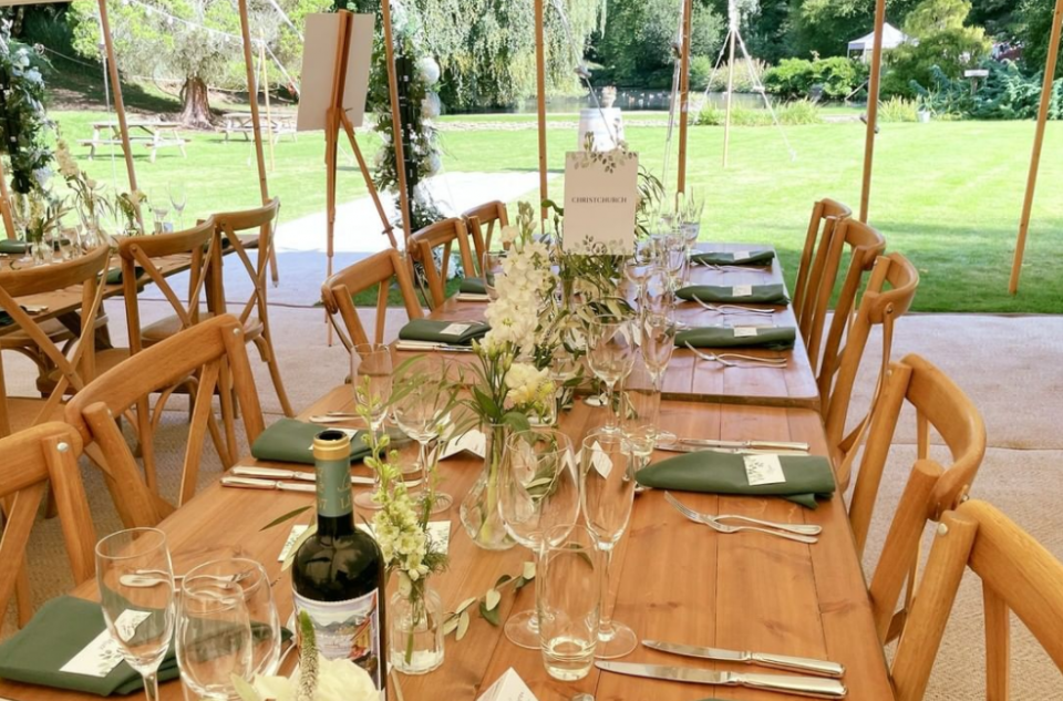 Bare wooden table and wooden chairs, green napkins and subtle flower arrangements