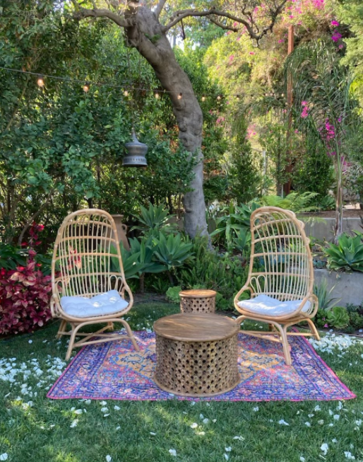 Chill out area with two wicker armchairs, wooden coffee table and colorful carpet under the tree with string lights